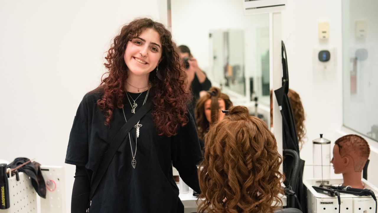 A Penn Commercial cosmetology student smiles for a picture while styling a head of hair