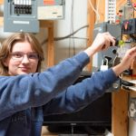 A Penn Commercial electrician student smiles at the camera while working on some wiring