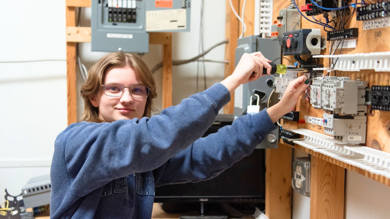 A Penn Commercial electrician student smiles at the camera while working on some wiring