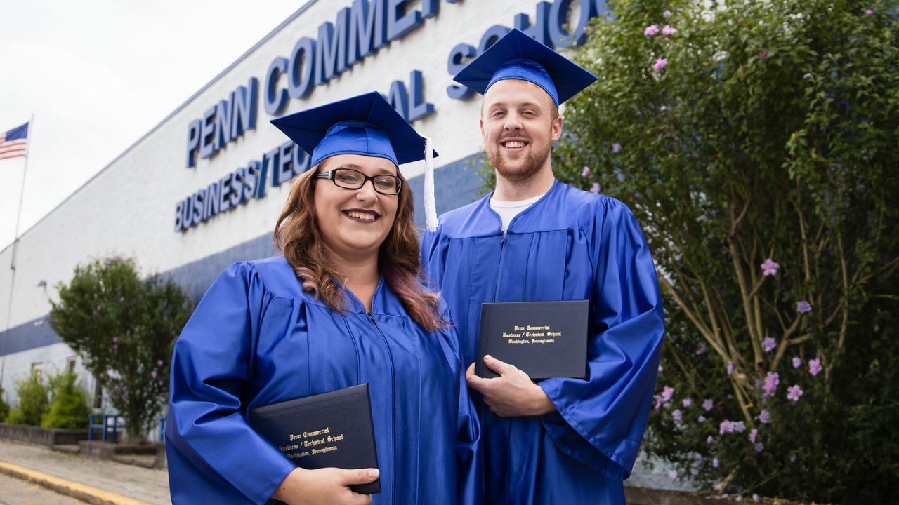 Two Penn Commercial graduates smile for a picture in front of the school