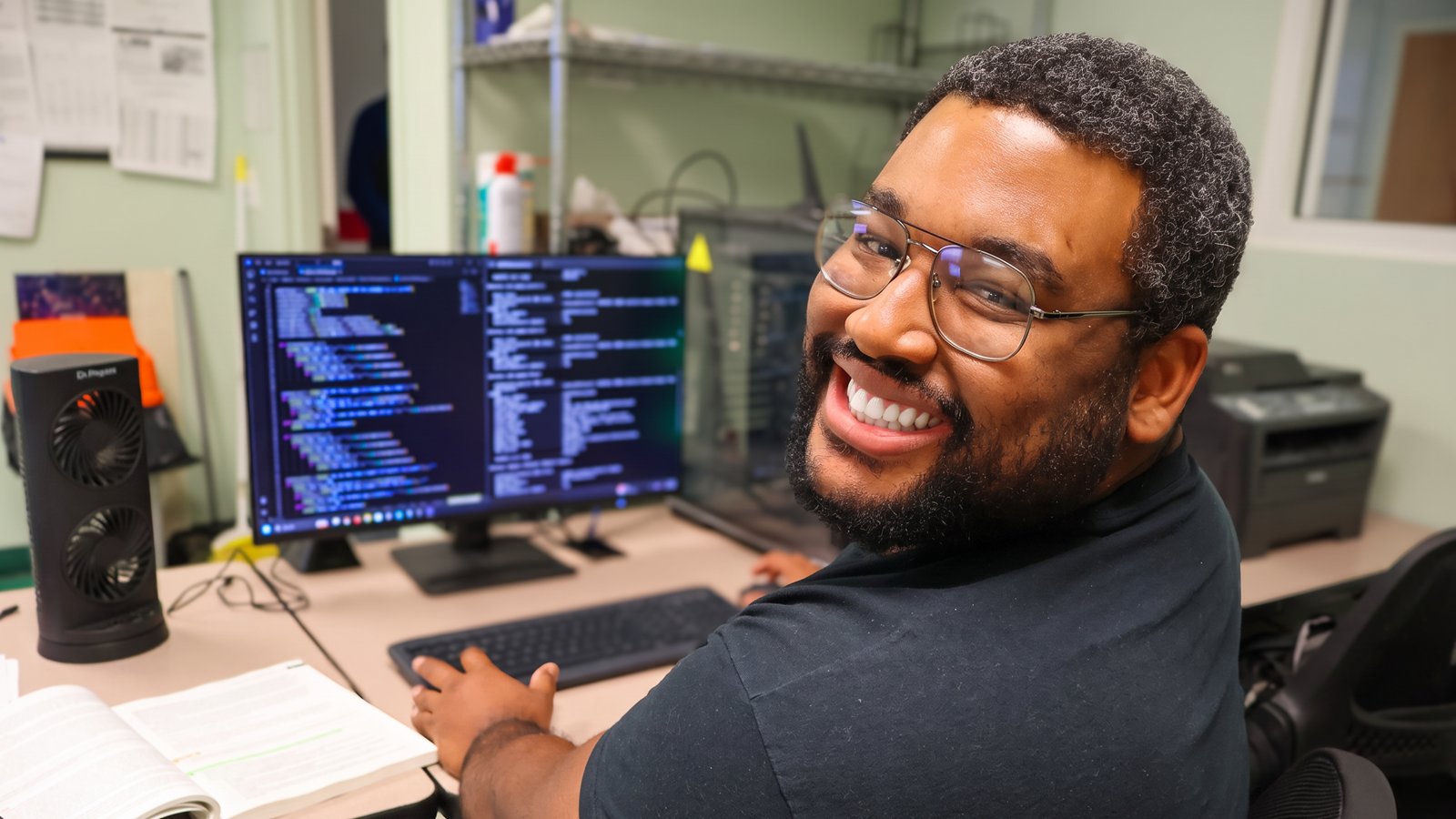 A smiling IT student at a computer workstation in Penn Commercial's lab.