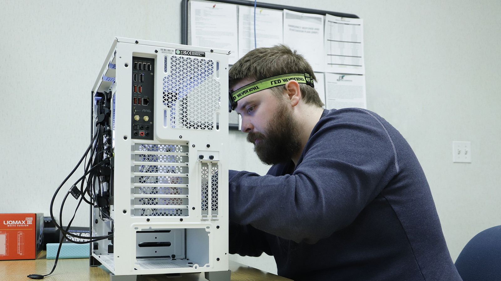 A Penn Commercial IT student wearing a headlamp works on the rear ports and cabling of a desktop computer.